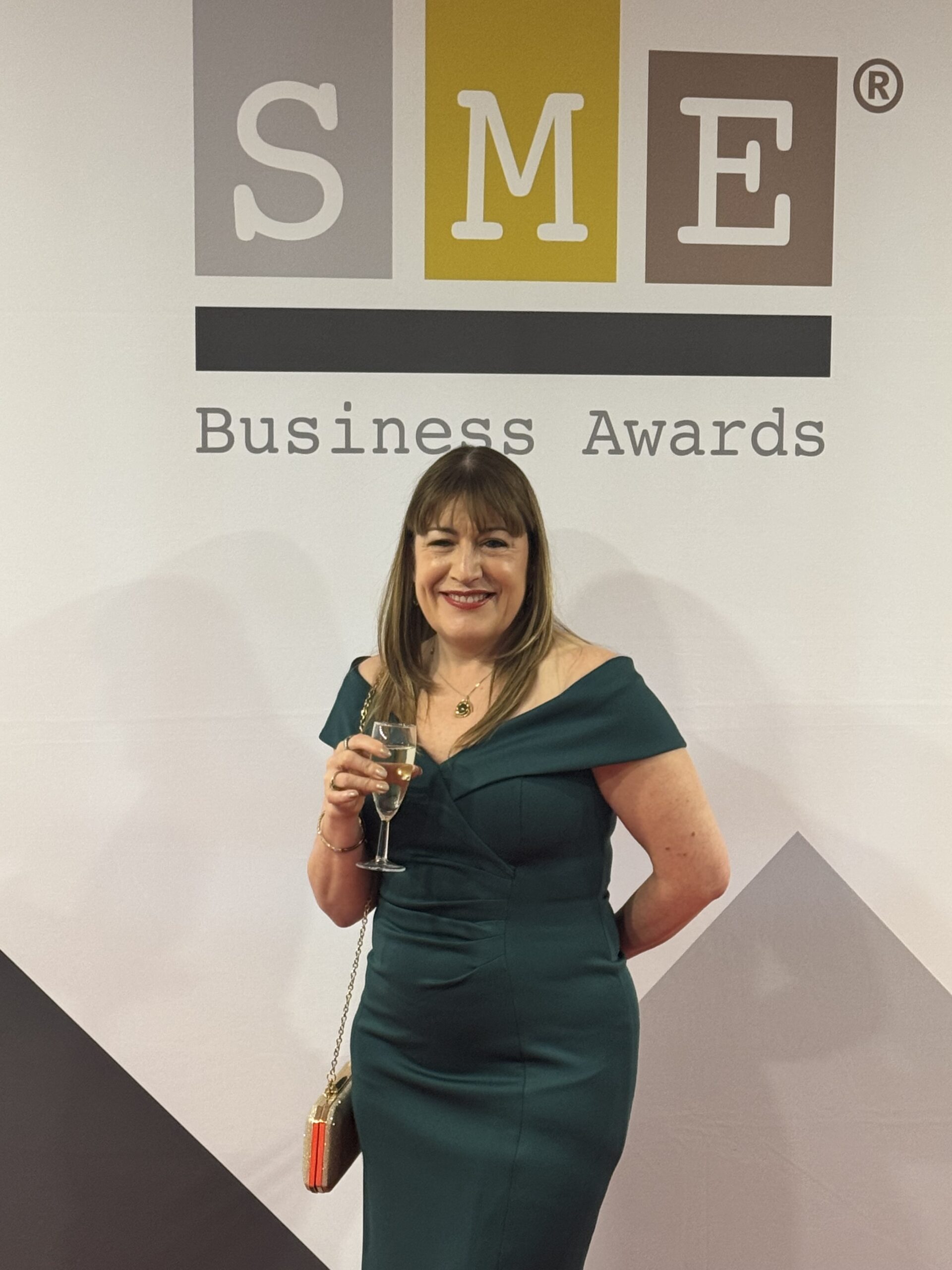 Antionette Oglethorpe standing in front of the SME Business Awards sign holding a glass of champagne
